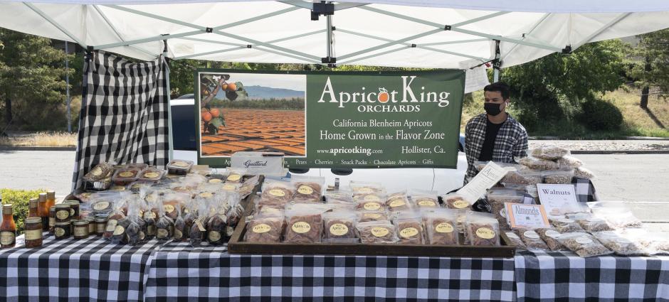 Apricot King vendor sitting at booth behind nuts and fruit spreads