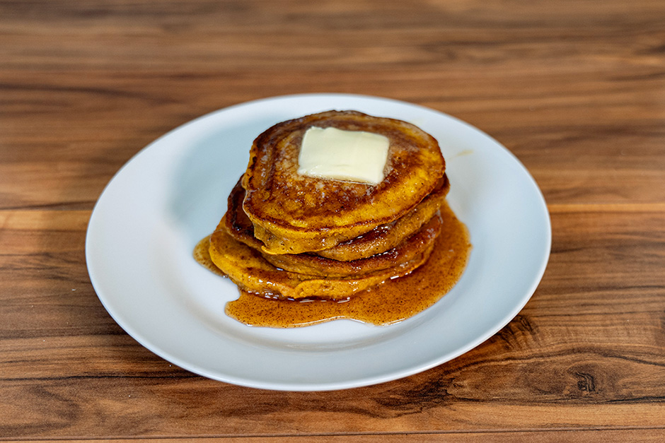 A stack of warm and delicious acorn squash pancakes on a white plate sitting on a wooden background