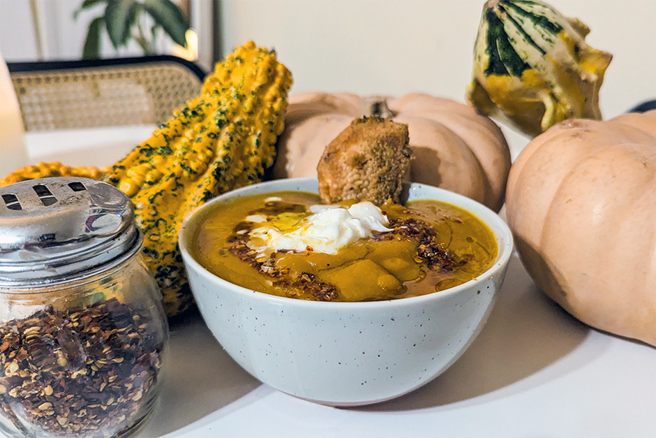 A bowl of orange butternut squash soup surrounded by gourds 