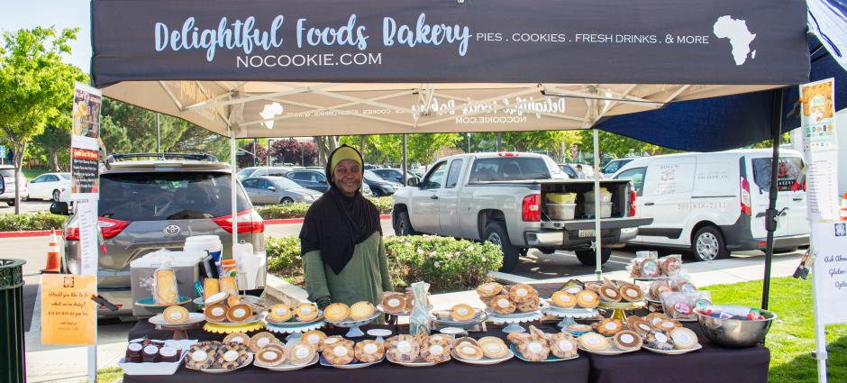 Owner of d=Delightful Foods smiling in booth surrounded by goods