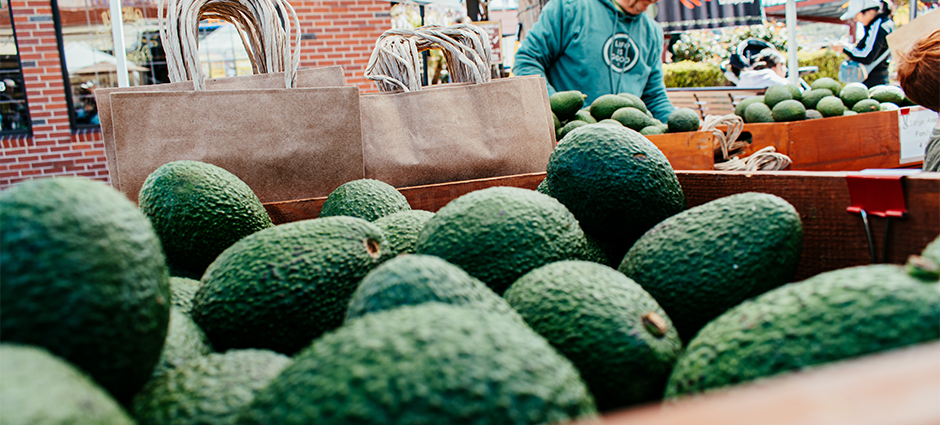 Photo with avocados in foreground and farmer in background