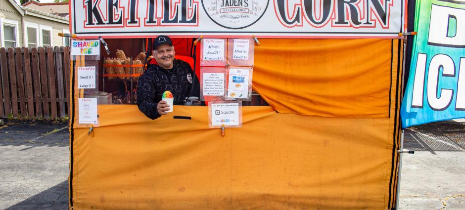 Photo of owner of Jaden's Kettle Corn handing snow cone out the window