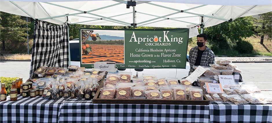 Apricot King vendor sitting at booth behind nuts and fruit spreads