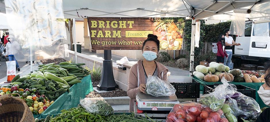 Bright Farm vendor behind table with various produce on display