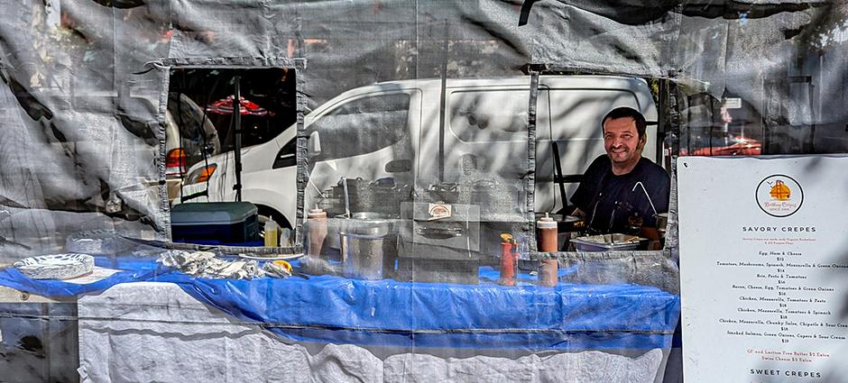 A man pokes his head out of netting at the Brittany Crepes stall at the Concord Farmers' Market