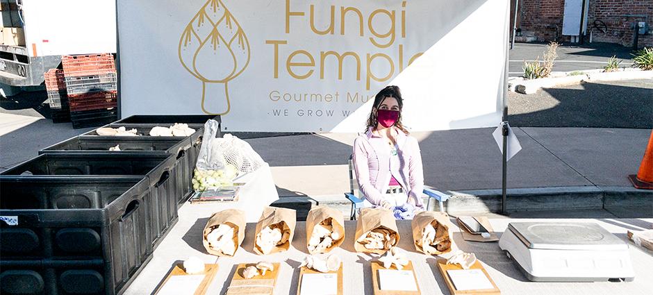 Fungi Temple vendor behind stall full of mushrooms