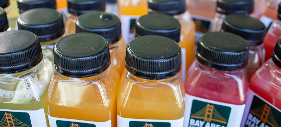 Bay Area Harvest bottles lines up displaying flavors. Vibrant colorful juices.
