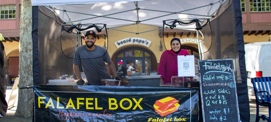 Smiling man and woman inside of the Falafel Box stall at the Concord Farmers' Market