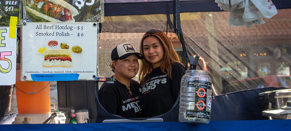 Two woman who own Meyer's BBQ looking through the window of their stall at the Concord Farmers' Market