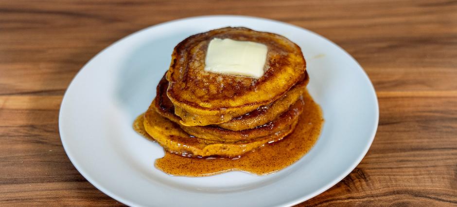 A stack of warm and delicious acorn squash pancakes on a white plate sitting on a wooden background