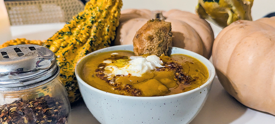 A bowl of orange butternut squash soup surrounded by gourds 